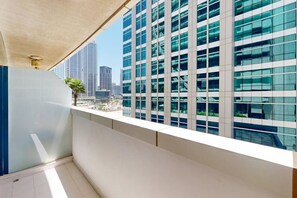 Un balcon avec vue sur des immeubles de grande hauteur, un palmier et un ciel dégagé.