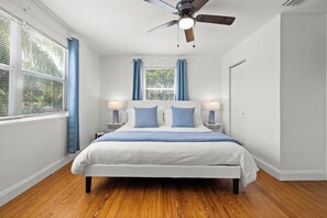 A bedroom with a bed, ceiling fan, window with blinds, and nightstands. - West Palm Beach Home (West Palm Beach)