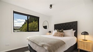 Un dormitorio con una cama grande, una ventana con vistas, un espejo redondo, una mesita de noche con una lámpara y un cabecero oscuro.