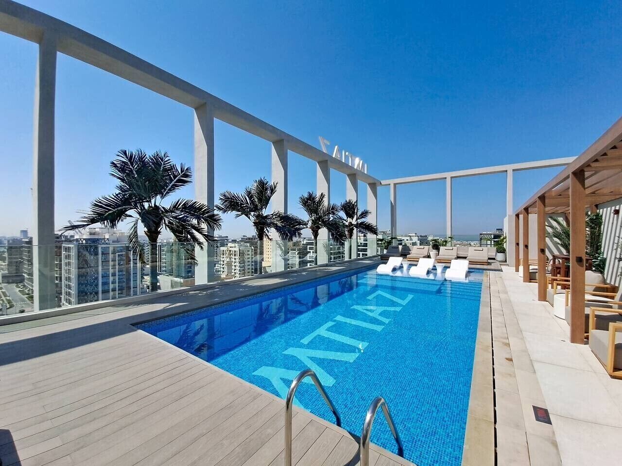 Ein Pool auf dem Dach mit klarem, blauem Wasser, umgeben von Palmen und Blick auf die Stadt.