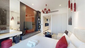 A modern hotel room with a large bed, a flat-screen TV, a seating area with a sofa and armchairs, a dining table, and a built-in bookshelf. - Premium Studio l near Museum of Future and Metro (Al Satwa)