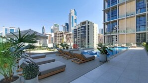 A rooftop pool area with lounge chairs, potted plants, and a view of modern buildings. - Premium Studio l near Museum of Future and Metro (Al Satwa)