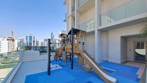 A rooftop playground with a slide and climbing structures, surrounded by a modern building with large windows. - Premium Studio l near Museum of Future and Metro (Al Satwa)