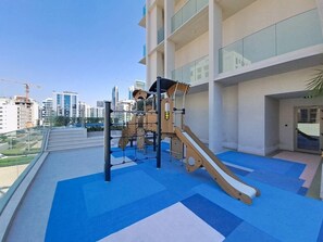 A rooftop playground with a slide and climbing structures, surrounded by a modern building with large windows. - Premium Studio l near Museum of Future and Metro (Al Satwa)