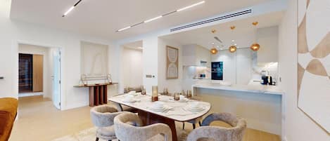 Uma área de jantar moderna com uma mesa redonda, seis cadeiras e uma cozinha ao fundo.