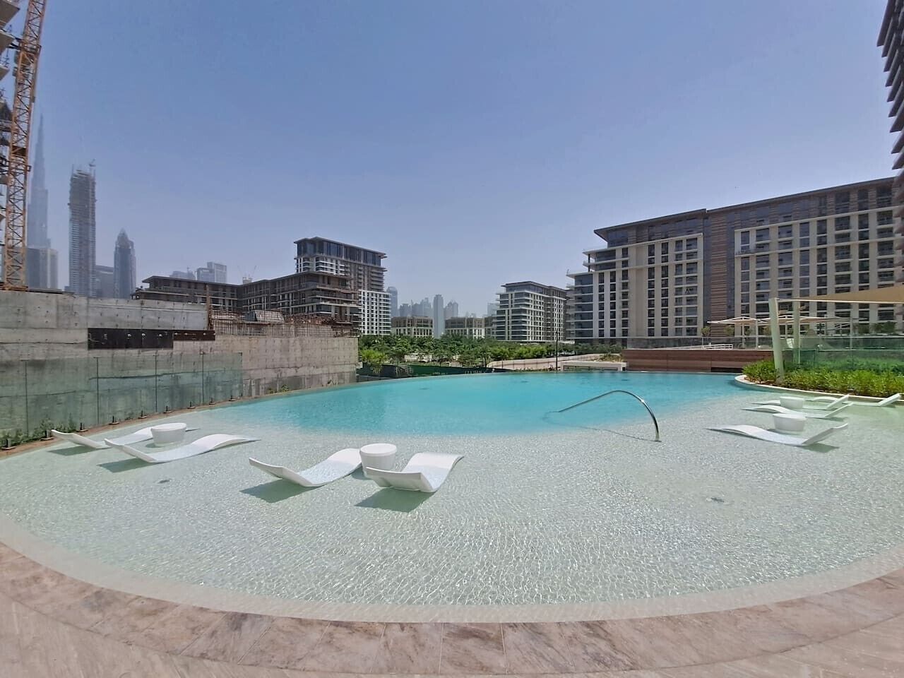 A rooftop pool with lounge chairs, a diving board, and a view of surrounding high-rise buildings.