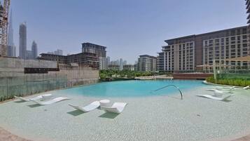 A rooftop pool with lounge chairs, a diving board, and a view of surrounding high-rise buildings.