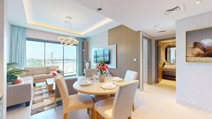 Una camera d'hotel moderna con zona pranzo, divano, TV e un'ampia finestra.
