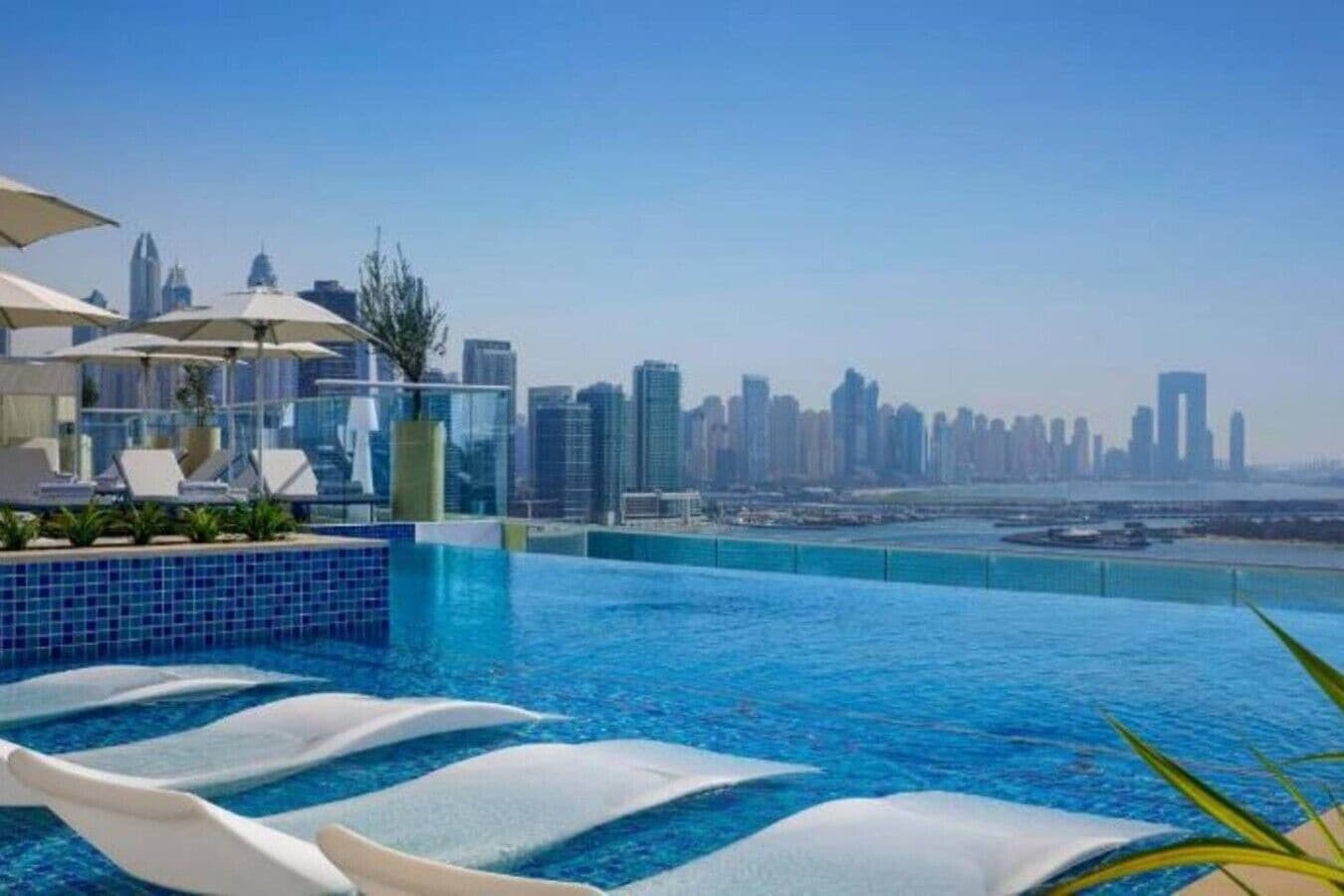 Una piscina infinita en la azotea con vista al horizonte de la ciudad, sillas de descanso y sombrillas.