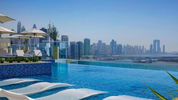 A rooftop infinity pool with a city skyline view, lounge chairs, and umbrellas. - Chic Studio in Palm l Pool & Gym (Palm Jumeirah)
