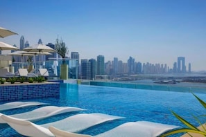 A rooftop infinity pool with a city skyline view, lounge chairs, and umbrellas. - Chic Studio in Palm l Pool & Gym (Palm Jumeirah)