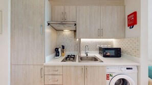 Uma cozinha compacta com micro-ondas, torradeira, pia e máquina de lavar.