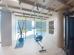 Un gimnasio moderno con equipo de ejercicio, amplias ventanas y vistas a edificios.