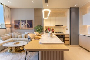 A modern kitchen with a central island, a dining area with a sofa, and a city view. - Luxe 1 Bed with Private Pool l Tennis Court (JVC)