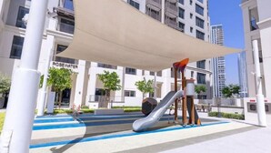 Un parc infantil amb tobogan i elements per escalar, envoltat d'una zona coberta amb un toldo.