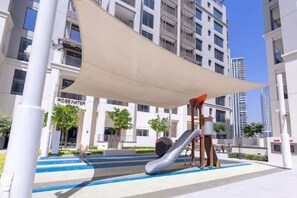 Ein Spielplatz mit Rutsche und Klettergerüsten, umgeben von einem überdachten Bereich mit Sonnensegel.
