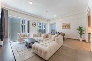 A spacious living room with a large sectional sofa, a coffee table, and a dining area with chairs and a table. - Sleek 3 Bed in Creek Harbour l Private Lagoon, Gym (Creek Harbour)