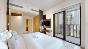 Ein Hotelzimmer mit einem großen Bett, einem an der Wand montierten Fernseher, einer Schiebetür zum Balkon und einem durch eine offene Tür sichtbaren Badezimmer.