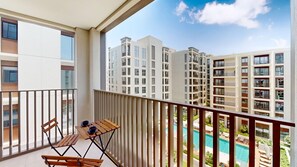 A balcony with a table and chairs, overlooking a swimming pool and high-rise buildings. - Sleek 3 Bed in Creek Harbour l Private Lagoon, Gym (Creek Harbour)