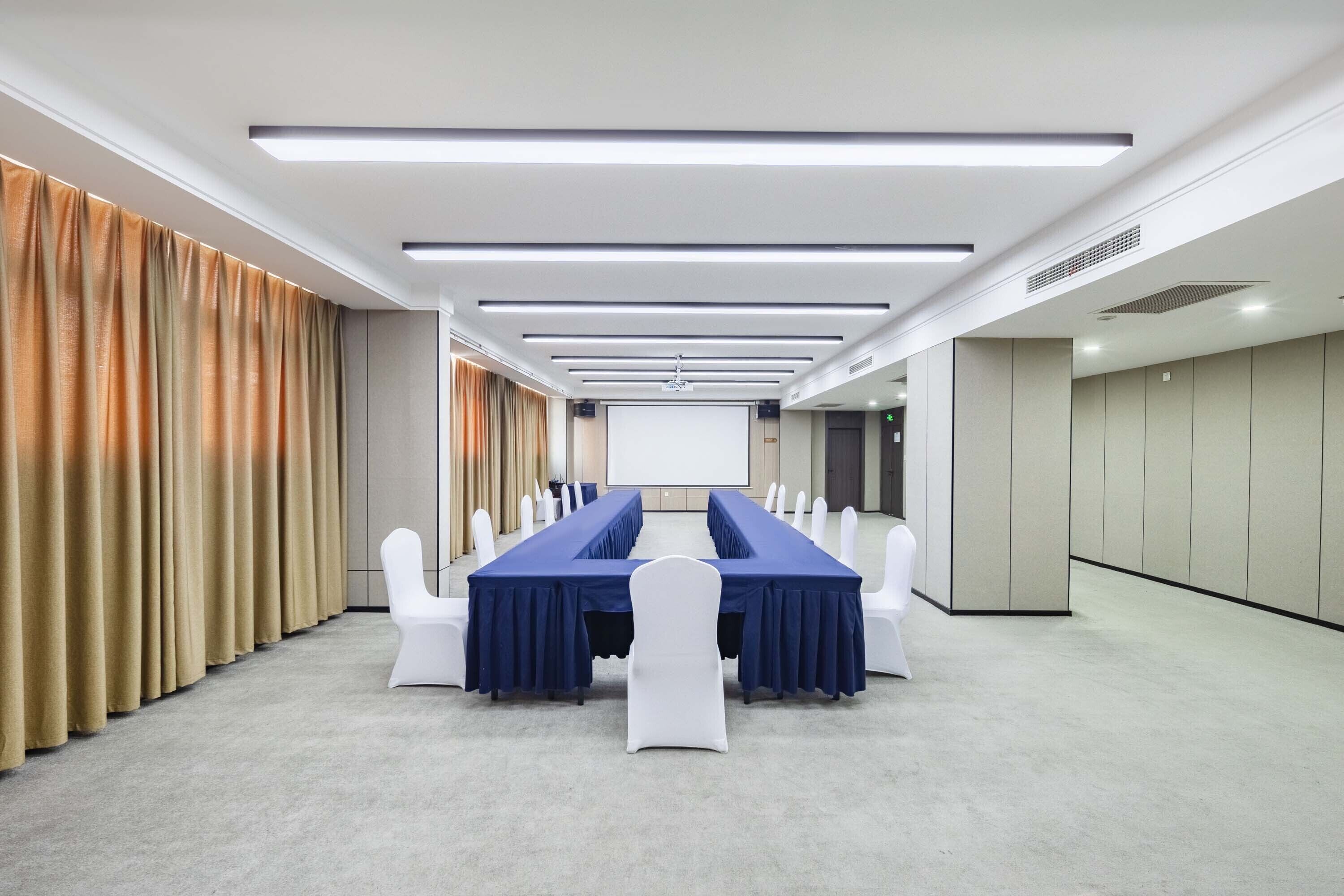 A conference room with a long table, white chairs, and a projector screen.