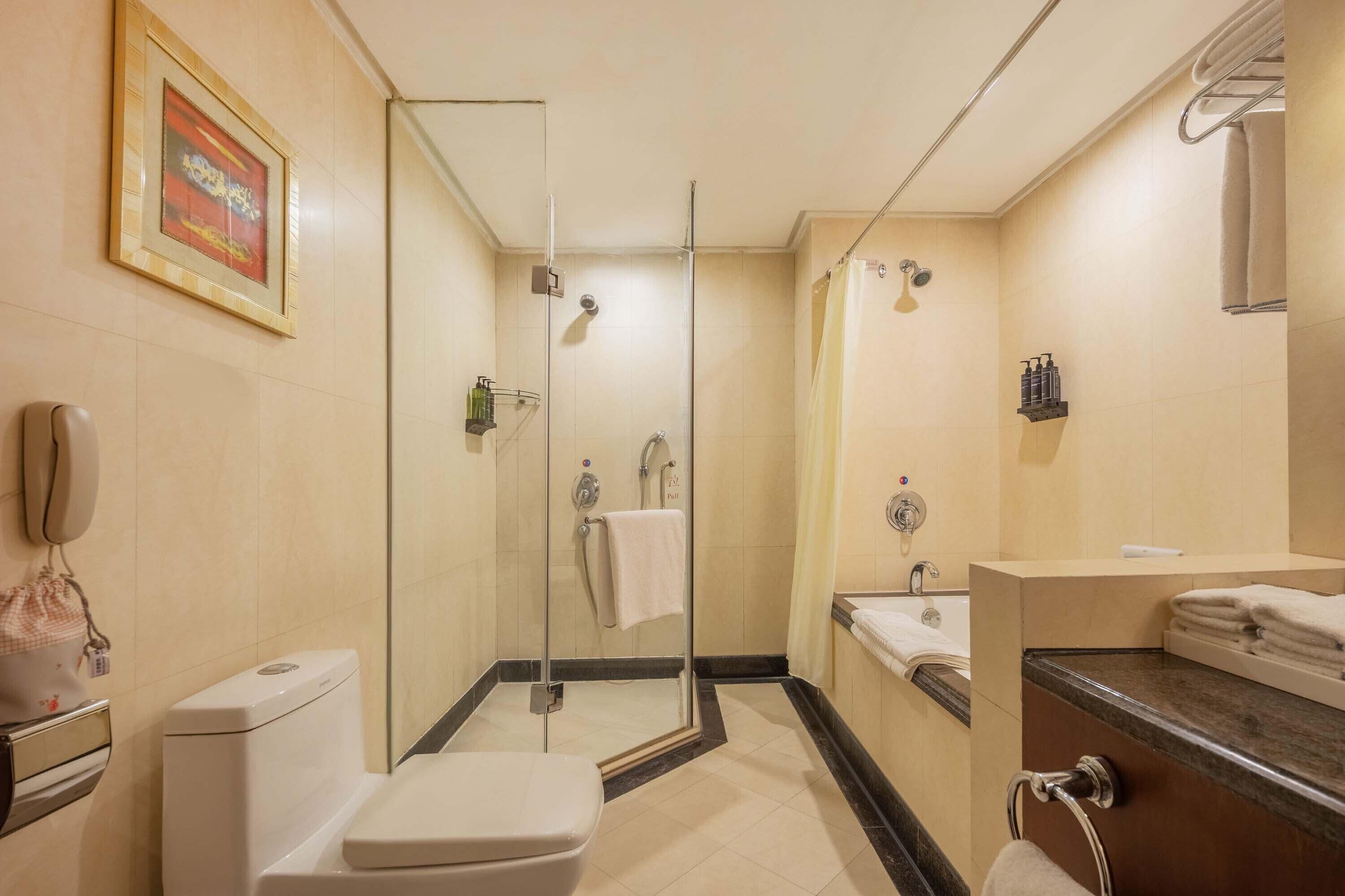 A hotel bathroom with a glass-enclosed shower, a toilet, a sink with a mirror, and a towel rack.