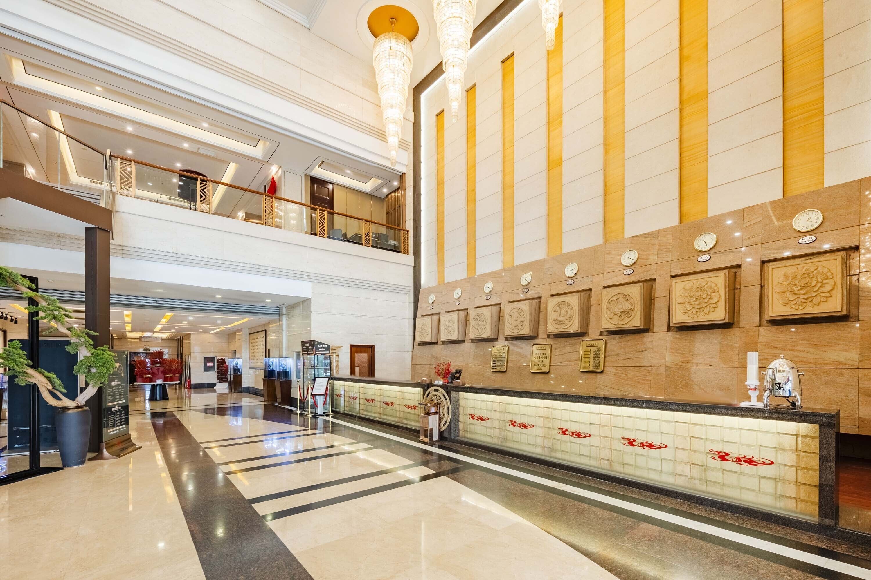 A spacious lobby with a reception desk, a plant, and a high ceiling with chandeliers.