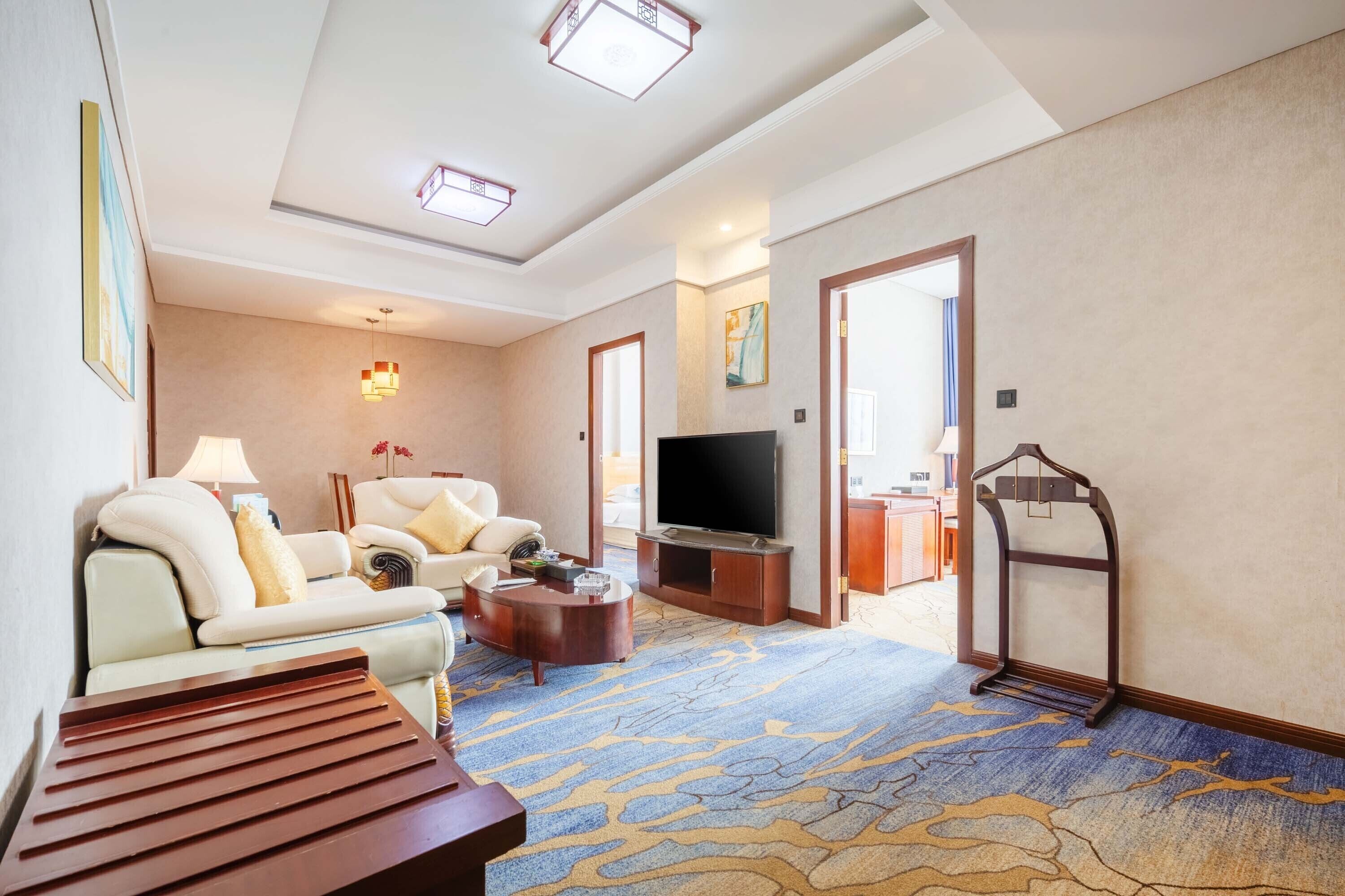 Habitación de hotel con sofá, televisión y alfombra estampada.