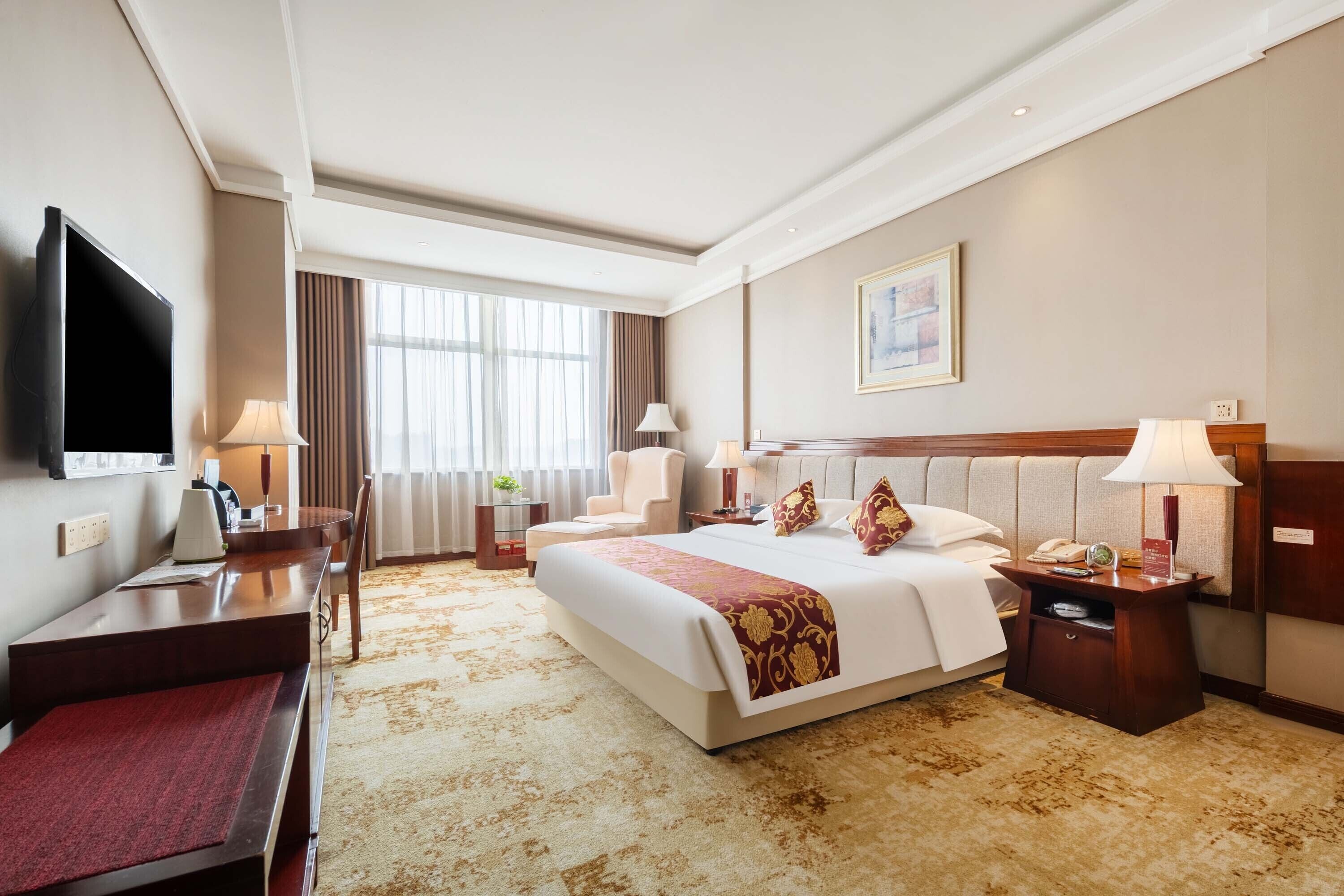 A hotel room with a large bed, a desk, a television, and a window with curtains.