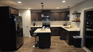 A modern kitchen with dark cabinets, stainless steel appliances, a central island, and a hanging light fixture.