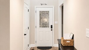 A hallway with a wooden floor, a white door with a frosted glass window, and a small table with a basket.