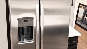 A stainless steel refrigerator with a built-in water dispenser, a dark wooden cabinet above it, and a black leather chair in the foreground.