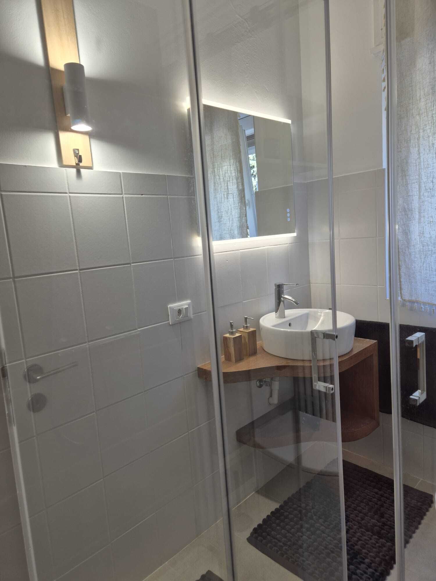 Une salle de bain moderne avec une douche à parois de verre, un lavabo blanc et un meuble-lavabo en bois.