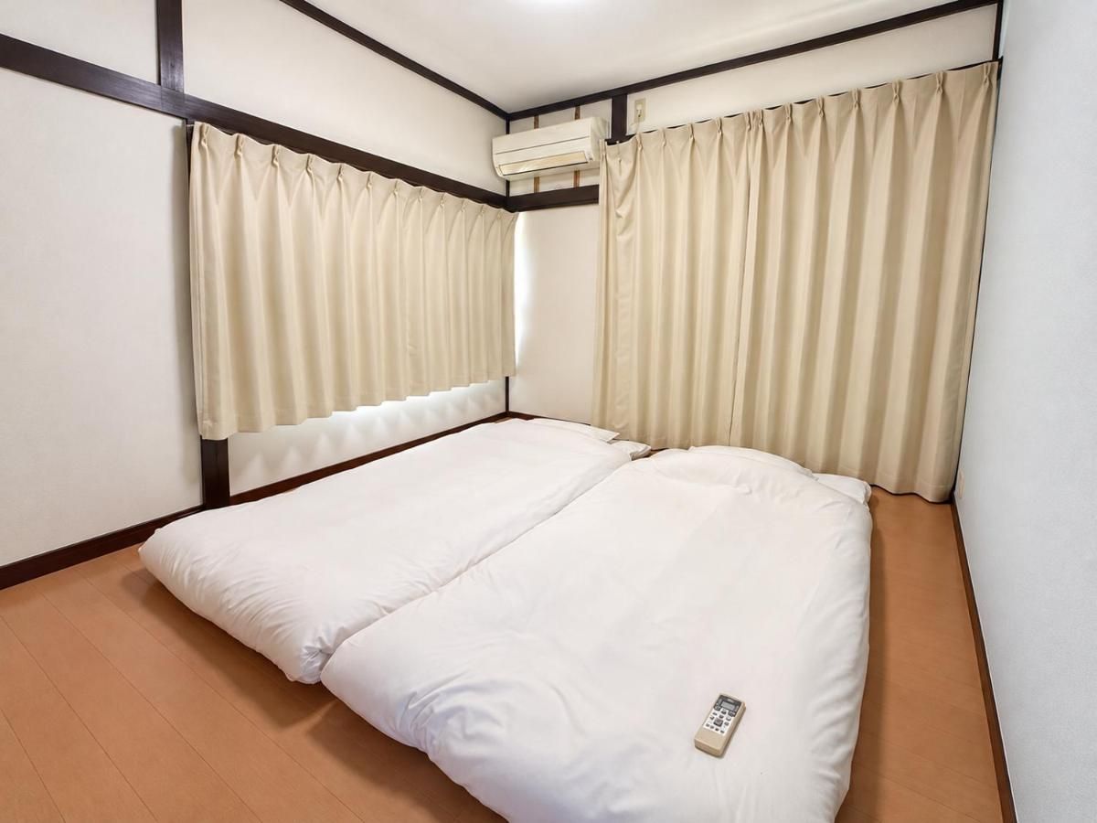 A single bed with a white mattress and pillows, beige curtains, and a wall-mounted air conditioning unit.