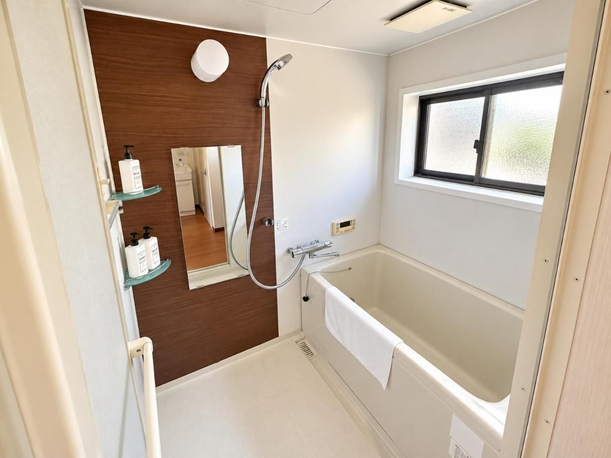 A bathroom with a bathtub, a shower, a mirror, and a window.