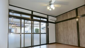 A room with a large sliding glass door, a ceiling fan, and an air conditioning unit. - EASE Takasaki Toyooka (Takasaki)
