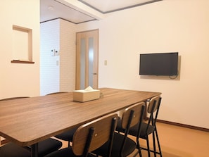 Ein Konferenzraum mit einem langen Tisch, vier Stühlen, einem Fernseher an der Wand und einer Tür zu einem weiteren Raum.