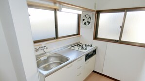 A compact kitchen with a sink, stove, and a window fan. - EASE Takasaki Toyooka (Takasaki)
