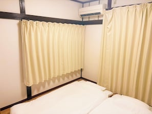 Ein Einzelbett mit weißer Bettwäsche, an beiden Seiten von je einem Vorhang eingerahmt.