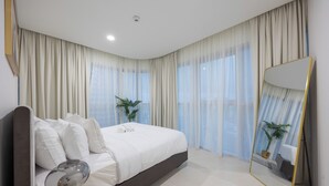 A modern bedroom with a large bed, a bedside table, a mirror, and sheer curtains. - Bloomfields 3BR - Radiant Viewz 2 - Reem (Abu Dhabi)