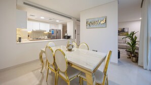 A modern dining area with a marble table, gold chairs, and a kitchen in the background. - Bloomfields 3BR - Radiant Viewz 2 - Reem (Abu Dhabi)