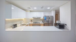 A modern kitchen with white cabinetry, a stainless steel refrigerator, a microwave, and a gas stove. - Bloomfields 3BR - Radiant Viewz 2 - Reem (Abu Dhabi)