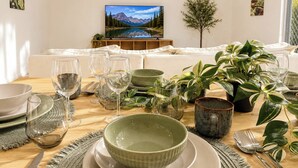 A dining area with a table set for four, a television displaying a mountain landscape, and a sofa in the background.