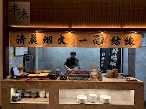 A restaurant counter with a chef preparing food, a variety of dishes displayed, and traditional Chinese writing on the walls. - Deqing Radisson Manor (Huzhou)