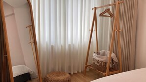 Un dormitorio con una cama de madera, un sillón colgante con cojín, un espejo y una ventana con cortinas de encaje.