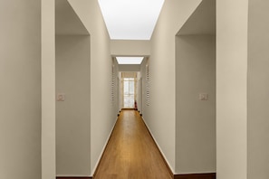 A long, narrow hallway with wooden flooring and white walls, leading to a room with a large window and a door. - Classic Sarvar Hospitality (Bengaluru)