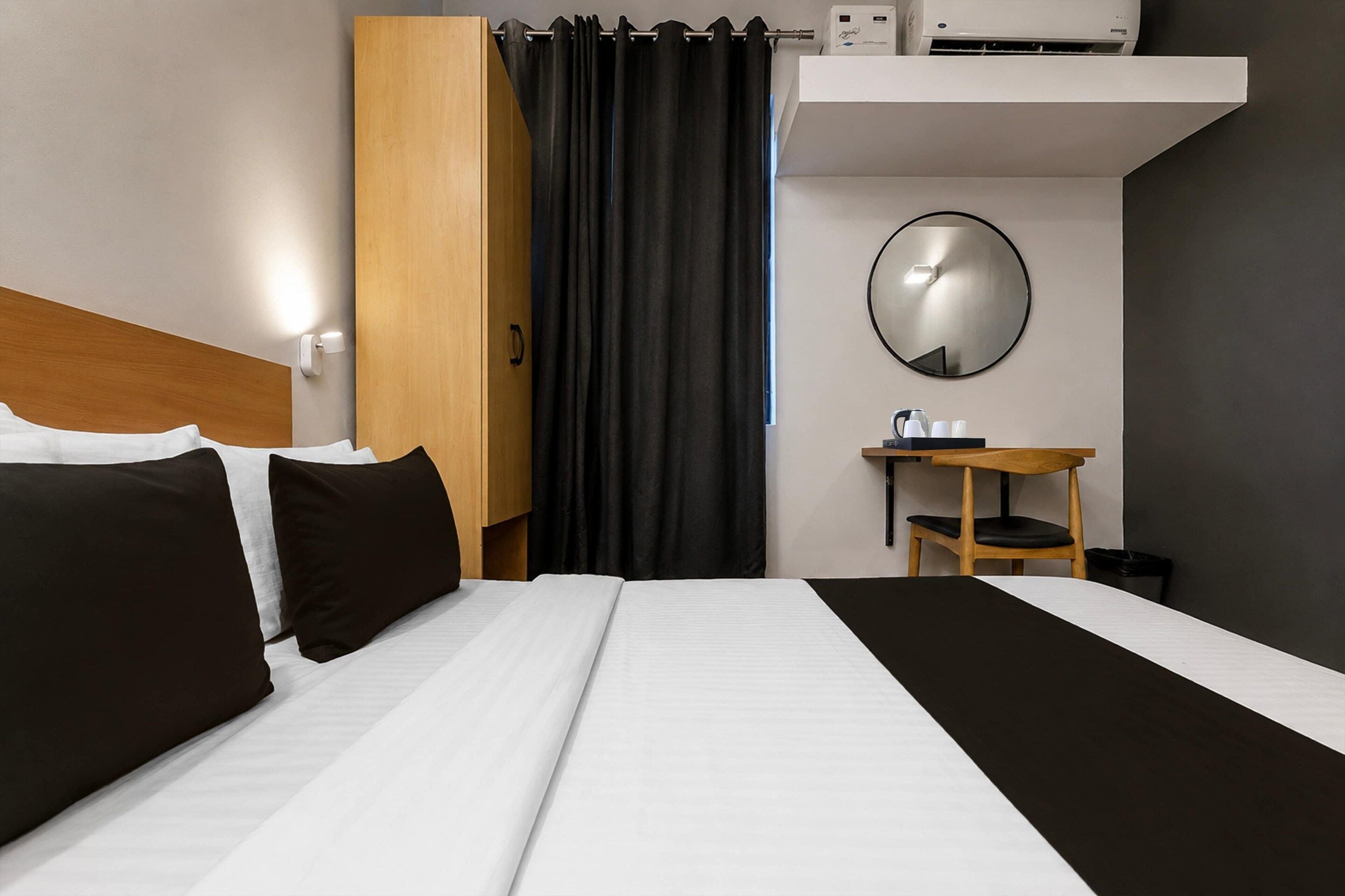 A hotel room with a bed, a bedside table, a mirror, and a wall-mounted air conditioning unit.
