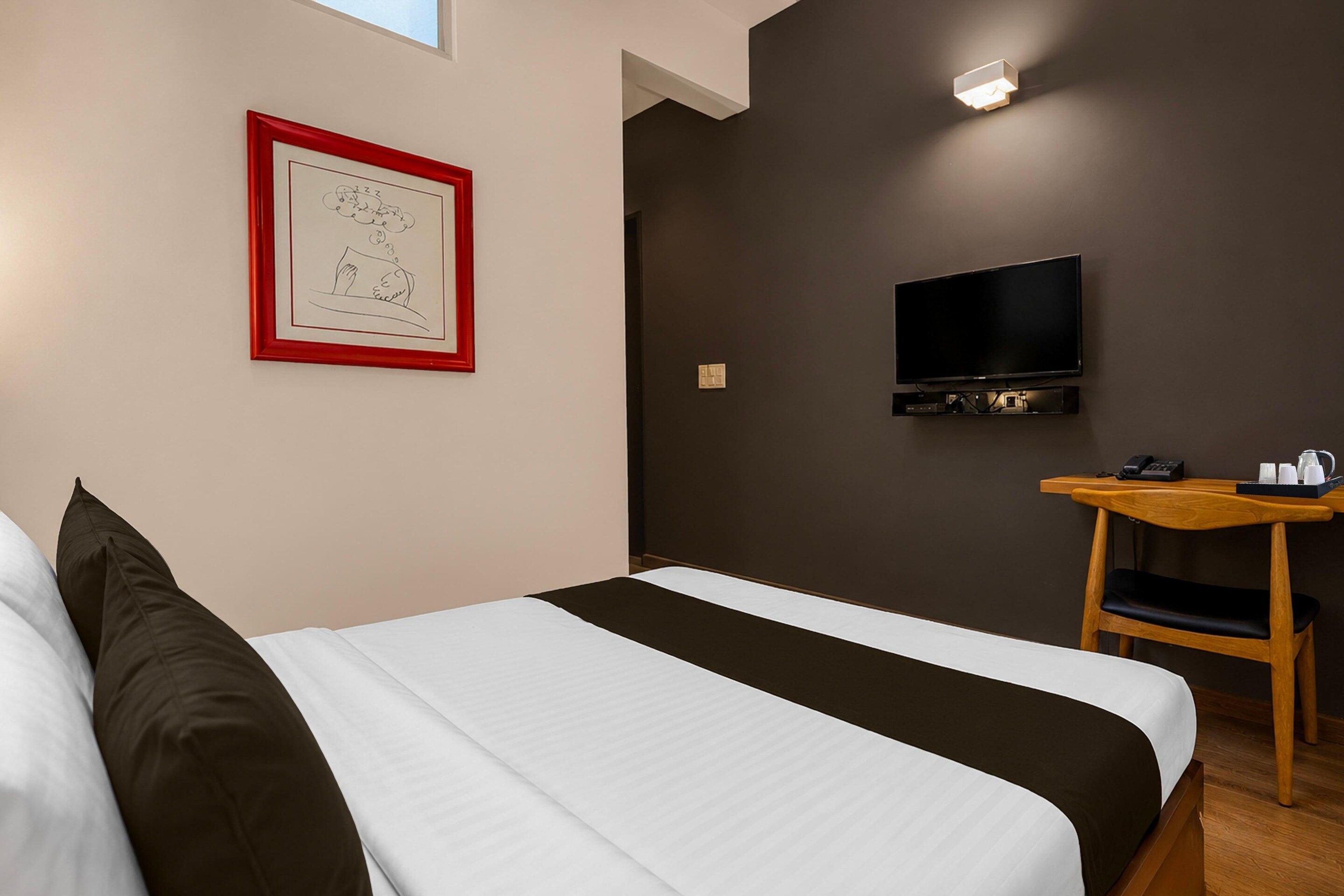 A hotel room with a bed, a TV, a desk, and a framed picture on the wall.