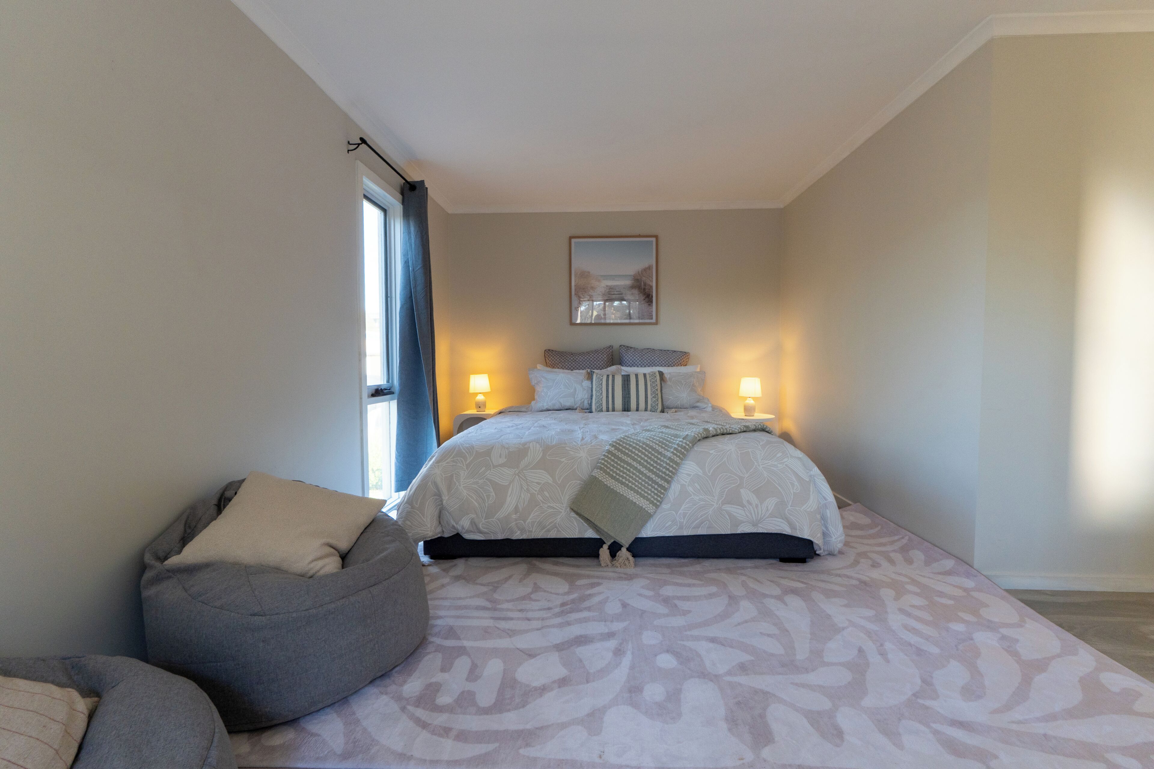 Ein Schlafzimmer mit einem Bett, Nachttischlampen, einem Sitzsack und einem gerahmten Bild an der Wand.