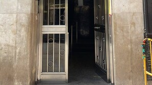 L'ingresso di un edificio con un cancello in metallo, un cartello sopra la porta e il numero '113' sulla parete.