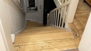 Una escalera de madera con barandilla blanca, un ventanal pequeño con diseño circular y una puerta al final.